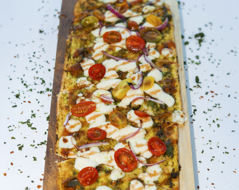 Benny's Coastal Kitchen puts a fresh spin on the caprese with its Caprese Flatbread. Fresh tomatoes, creamy mozzarella and basil are finished with pesto and a strawberry balsamic glaze for a bright, summery bite.