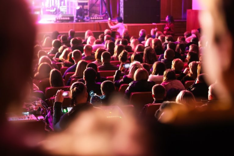 Spectators sit in the hall and watch a concert. People in the auditorium watching the performance. Theater audience. Music concert or festival. Out of focus.