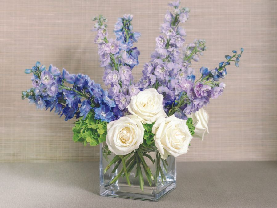 Floral arrangement with purples, blues, whites and greens in a glass vase