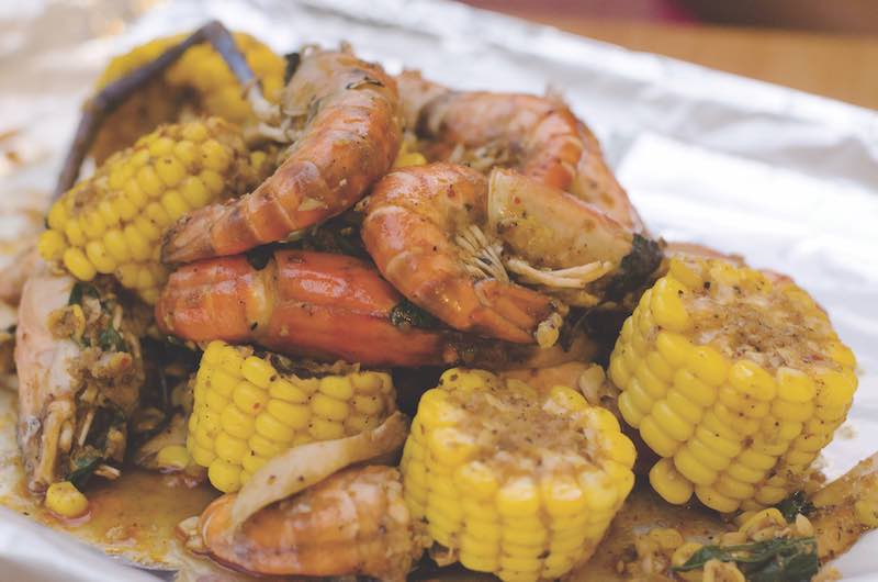 A tray is filled with corn on the cob, and shrimp. Everything is seasoned to perfection with spices.