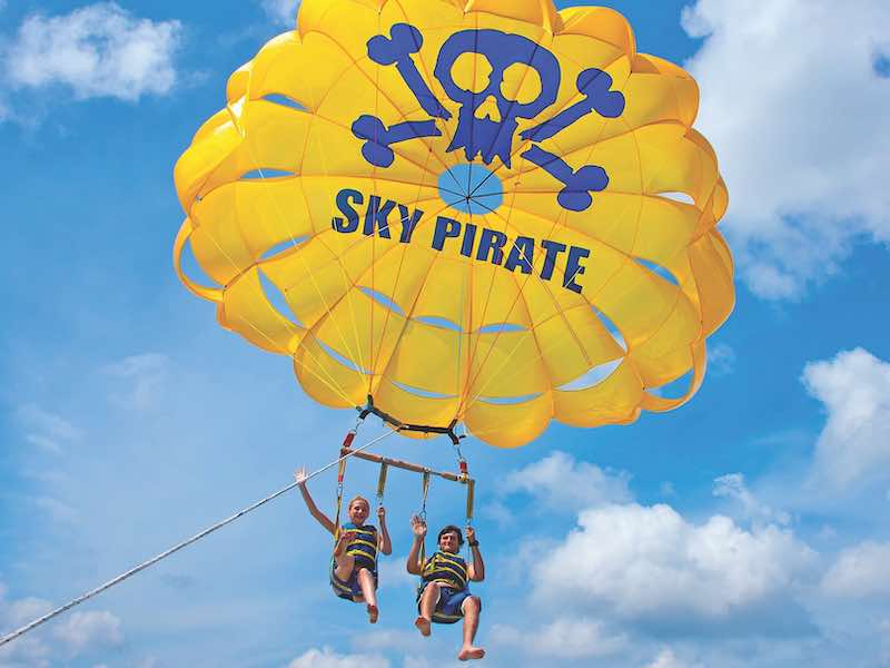Girl and a boy  parasailing - with a yellow parasail that says "Sky Pirate"