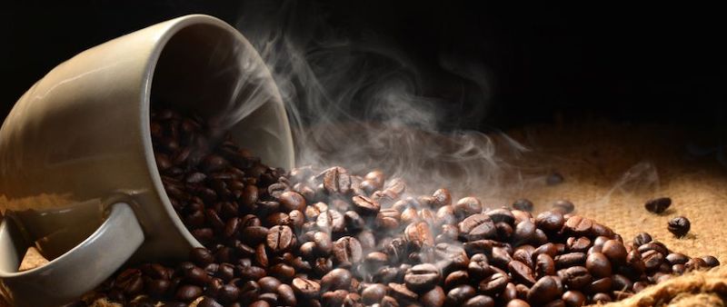 Coffee beans spilling out of a coffee cup with aroma in the air