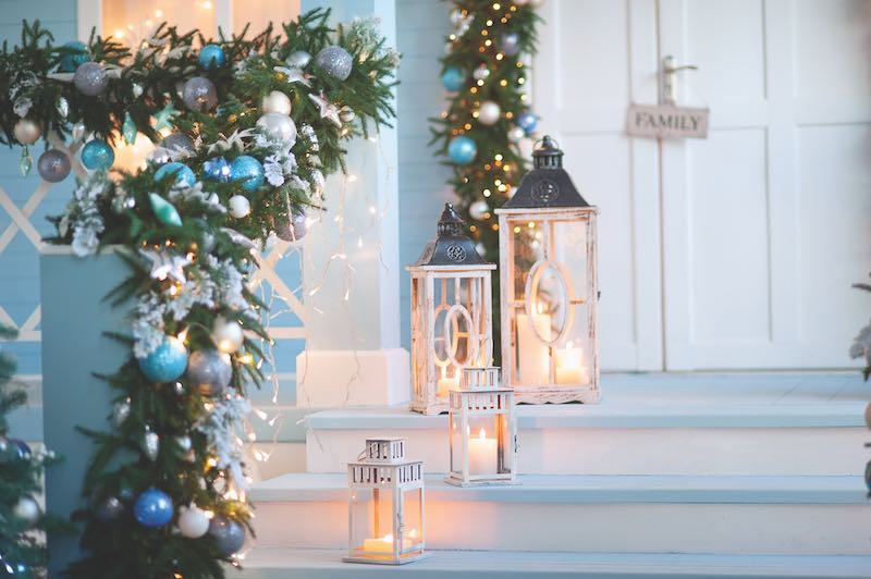 Blue ball ornaments in garland, with nearby white lanterns with glowing candles inside