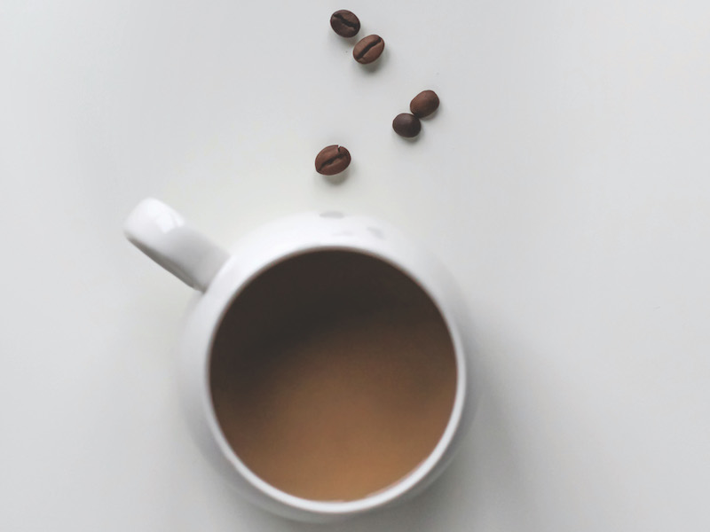 Cup of coffee overhead with coffee beans on a white surface