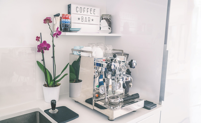 Home kitchen decor coffee bar for espresso machine on countertop, modern apartment living, wall shelves, orchid flower, indoor lifestyle.