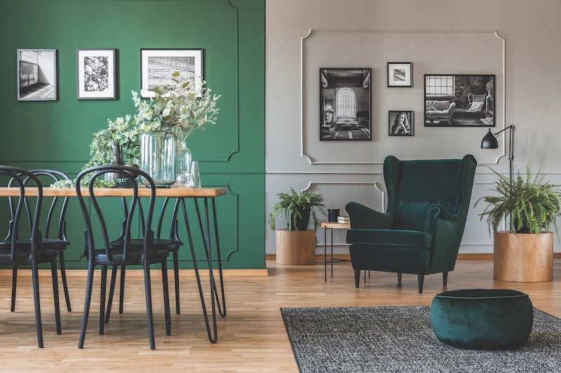 Elegant bottle green dining room with wooden table with black chairs and emerald green armchair and pouf