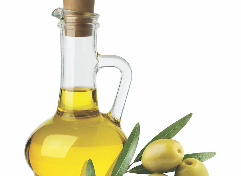 Delicious olive oil in a glass bottle and green olives with leaves, isolated on white background