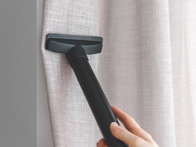 Cropped shot of employee hands with vacuum cleaner care about curtains in living room. Cleaning company staff steaming linen drapes on windows. Concept of anti allergenic measures at home