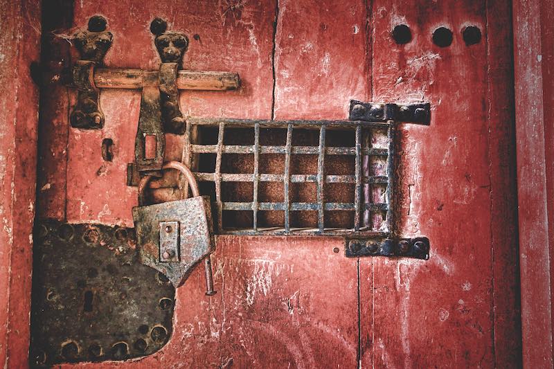 Old strong lock and cast iron latch locking hardware with speakeasy window on a medieval dungeon antique wood jail door