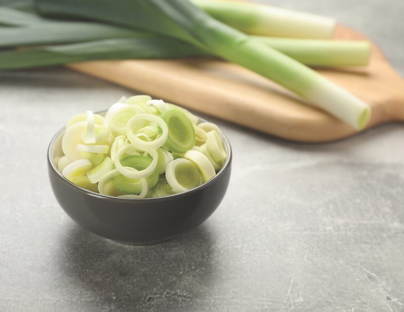 Cut fresh raw leek in bowl on grey table, space for text