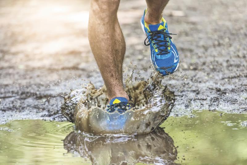 Running man walking in a puddle, splashing his shoes. Cross country trail. Freeze action