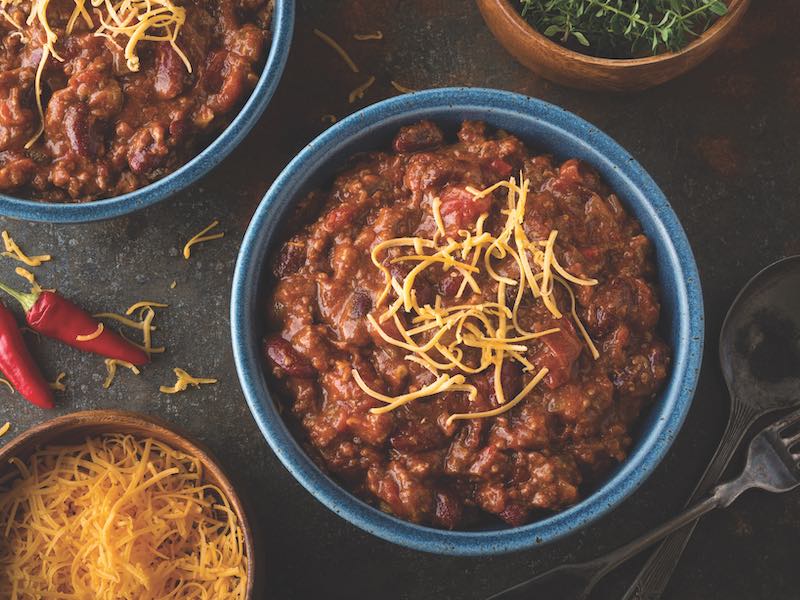 A bowl of delicious home made chili with ground beef, kidney beans, red pepper, tomato and shredded cheddar cheese.