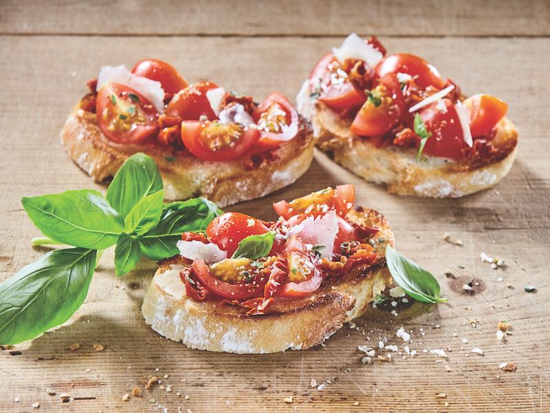Tasty tomato Italian bruschetta on toasted slices of baguette seasoned with spice and herbs and garnished with fresh basil on a wooden board with copy space, wide angle view