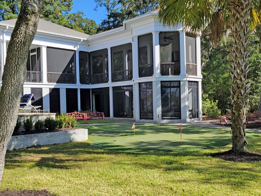 Back Exterior of a home with a large screened porch and golf putting green