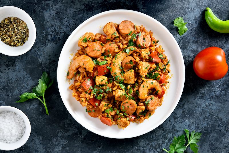 Creole jambalaya with rice, smoked sausages, chicken meat and vegetables on plate over blue stone background. Top view, flat lay, close up