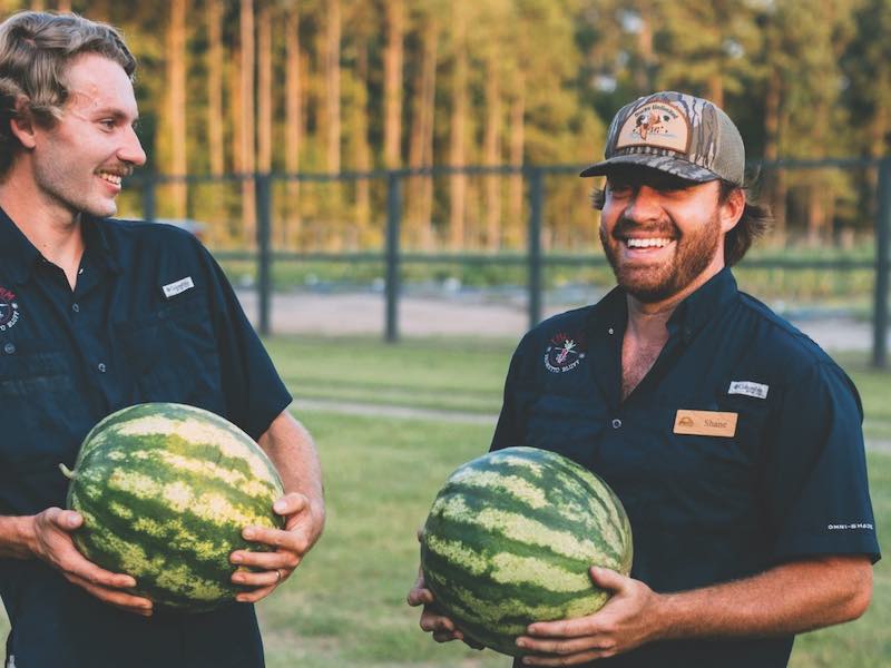 Two men holding watermelons at a farm