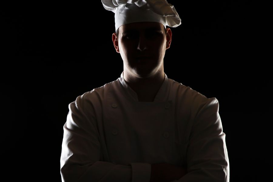Chef standing with his chef hat on and arms crossed - dark and moody background and editing