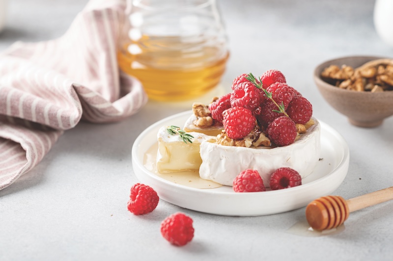 sliced brie cheese with raspberries, honey and walnuts . Selective focus, white background