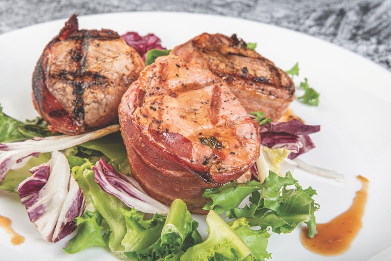 Pork tenderloin medallions, close-up. Grilled bbq steak wrapped in prosciutto
