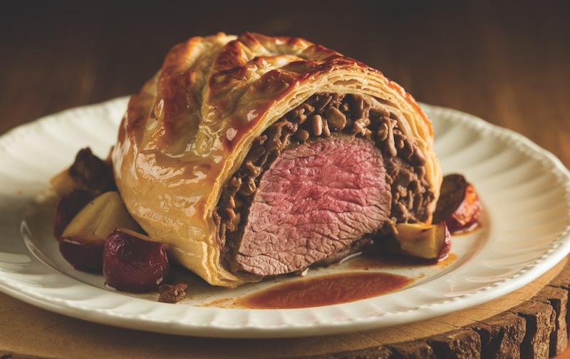 Beef Wellington: A tender beef fillet coated in mushroom duxelles, wrapped in puff pastry, and baked to golden perfection for a gourmet dish.