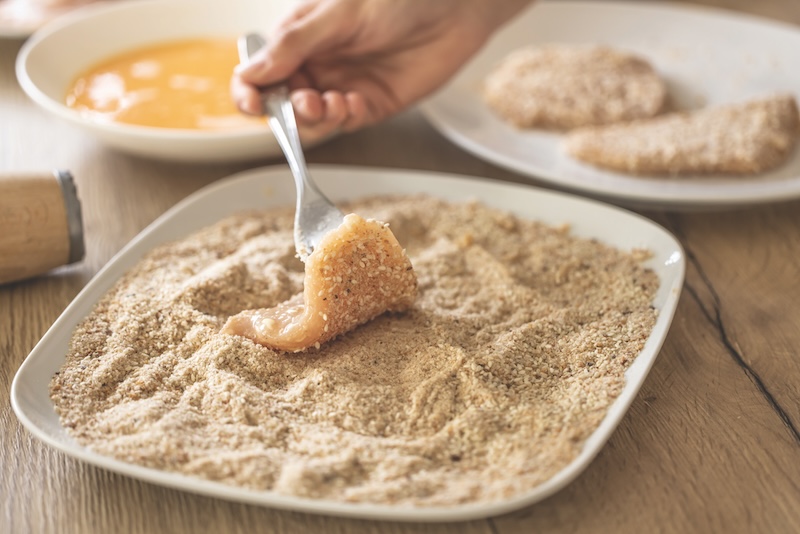 Final stage of coating meat in breadcrumbs while making schnitzels.
