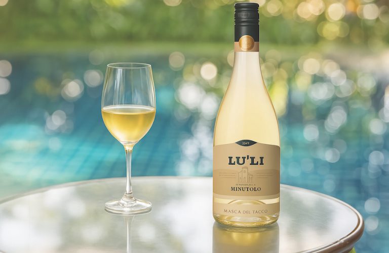 Bottle of Lu’Li Bianco pairs sitting next to a glass on wine on a table near a pool