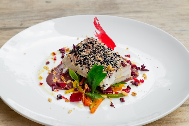 close up of a slow cooked , sous vide , tuna loin with black and white sesame crust, olive sauce, mixed vegetable and wine gelatine , white plate , natural light food photography, chef table inspired