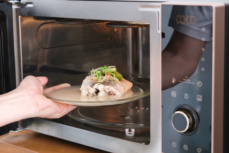 A housewife steaming fish in a microwave oven for a family dinner. She prepares it by putting fish dishes in the microwave and then serving healthy food. Cooking ideas