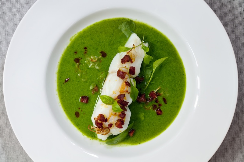 Butter poached cod with green peas, spinach and basil veloute, crispy chorizo and shallots