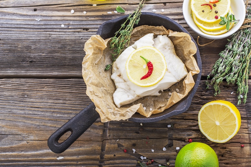 Cod fillets baked in parchment paper with slices of lemon and a sprig of thyme on light dishes. Selective focus. Concept of healthy food.