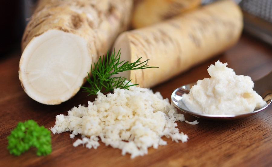 Grated horseradish with parsley on wooden table.