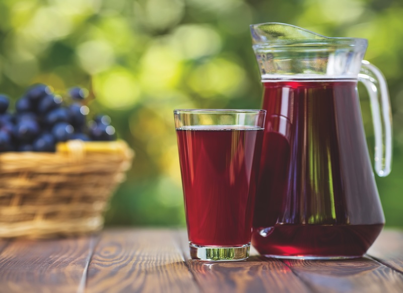fresh grape juice in glass and jug with ripe bunch of dark blue berries on wooden table outdoors