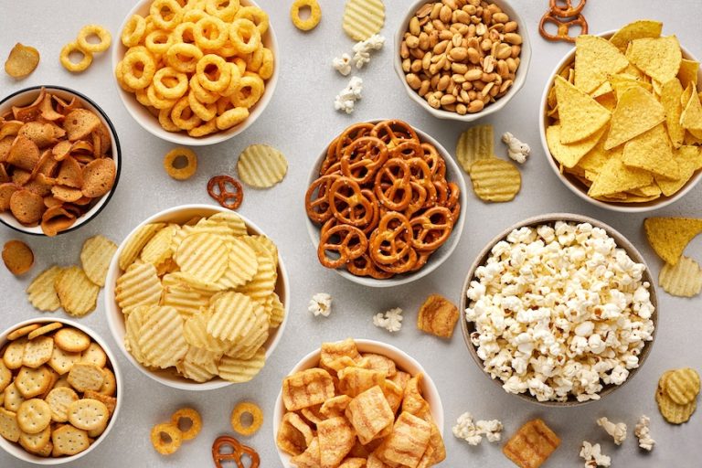 Set of many bowl with different salty snacks on light gray background. Chips, popcorn, nuts, nachos and pretzels. Party food. Top view