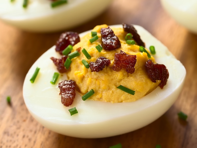 Deviled egg with bacon and chives, photographed with natural light (Selective Focus, Focus on the front of the egg yolk)