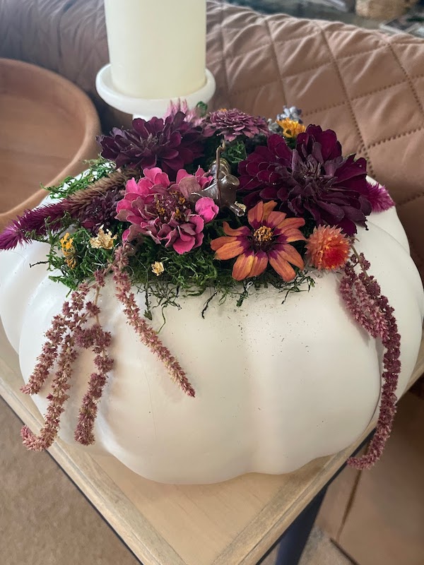 A white faux pumpkin is topped with a bouquet of flowers