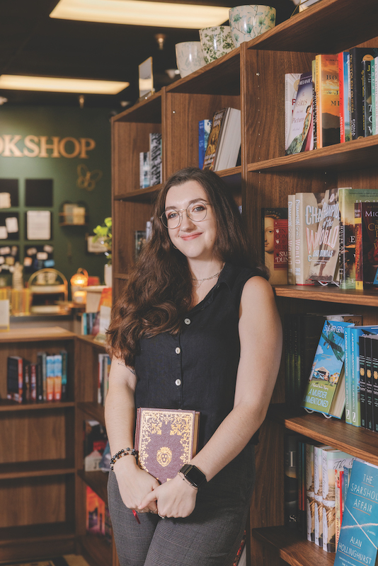 Emily Baker, co-owner of Emry's Bookshop, poses in front of the stocked shelves