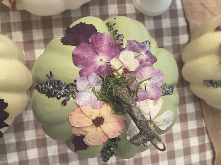 Green faux pumpkin is top with pressed pumpkins floral decor on gingham tablecloth
