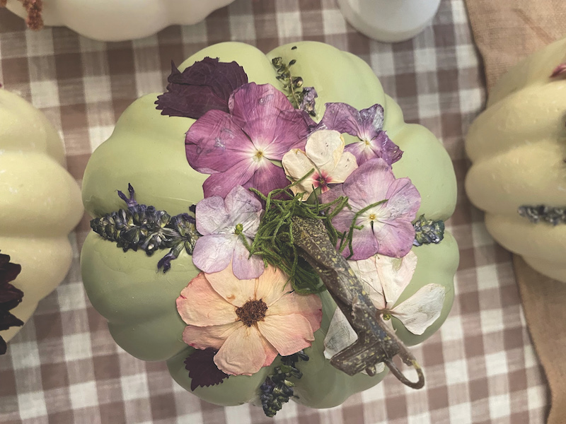Green faux pumpkin is top with pressed pumpkins floral decor on gingham tablecloth