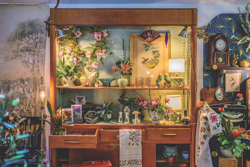 Branches display of antiques with decorative flowers, tea towels, ceramics, paintings and cabinet
