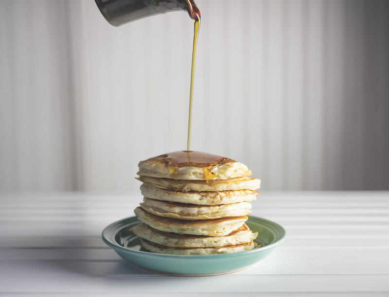 Pancakes stacked high with a generous pour of sweet sorghum syrup.