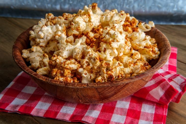 Seasoned spicy popcorn served in wooden bowl on rustic kitchen table