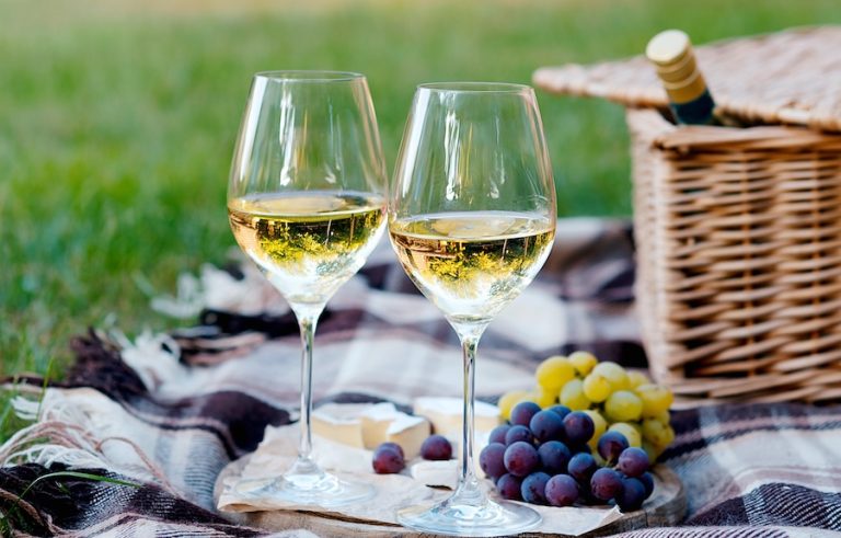 Two glasses of white wine and a wooden plate with cheese and grapes served outside