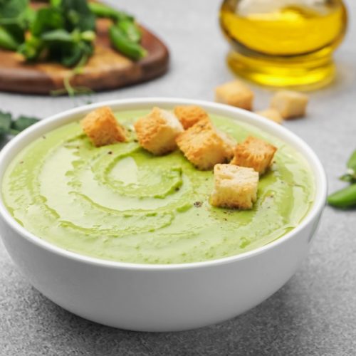 Tasty pea cream soup with croutons served on grey table, closeup