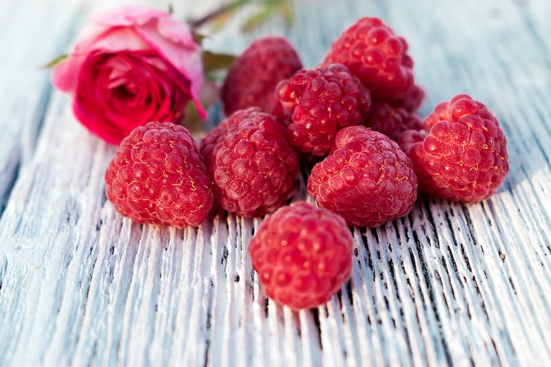 Raspberries and blurred pink rose on a white wooden background. Summer concept and concept of vitamin berries. Selective focus with shallow depth of field