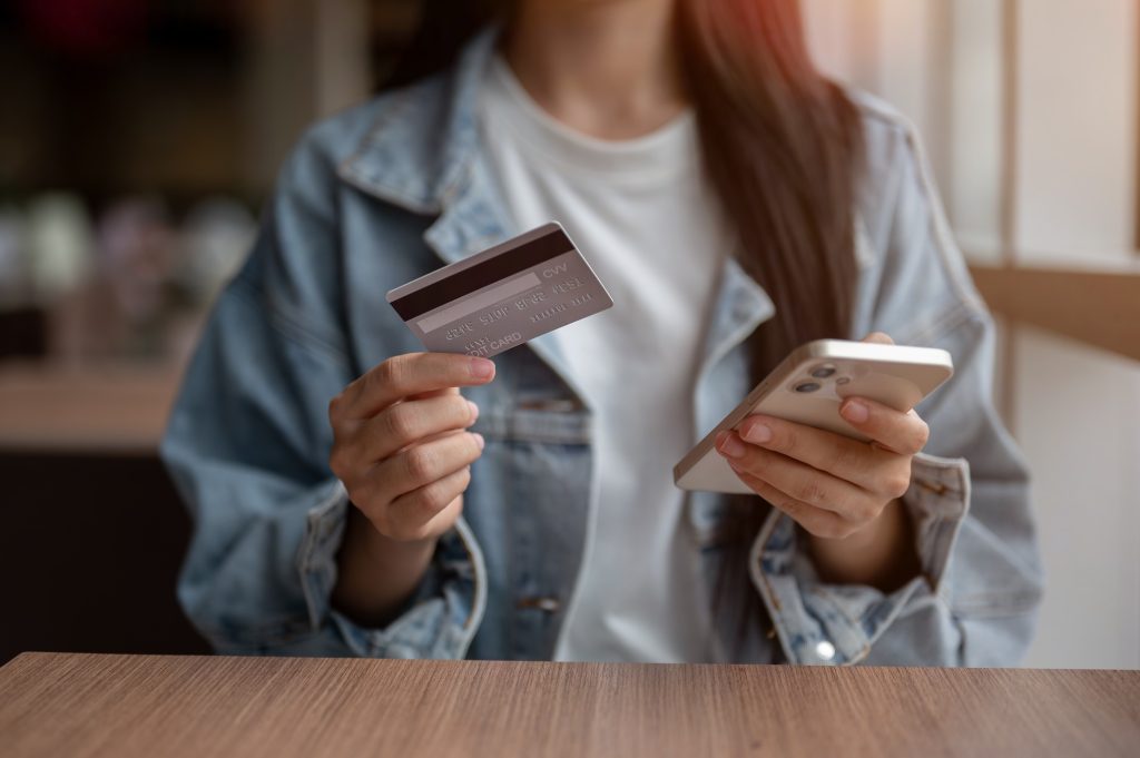 Close up of a woman's hand holding phone and credit card while sitting at table in cafe or lounge. Travel card, Cashless Society, Bank Advertising.