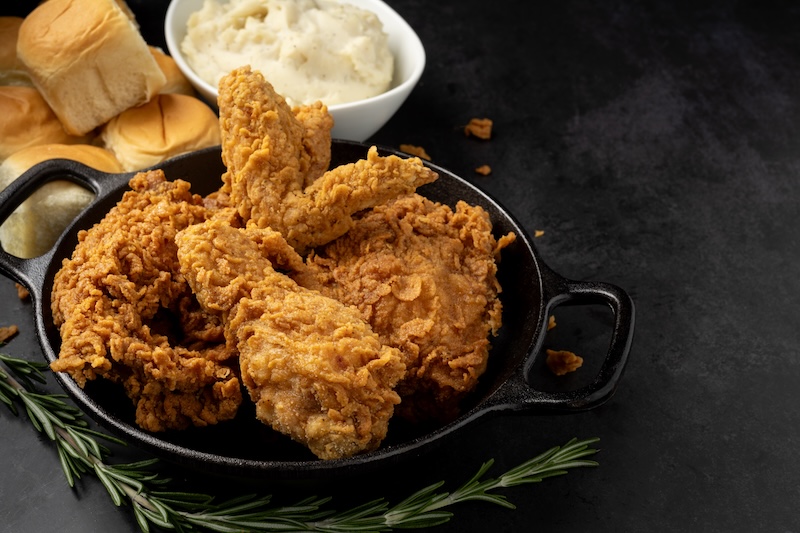 A 4-Piece Fried Chicken Meal with Leg, Wing, Breast and Thigh. Set on a small cast iron skillet and served with mashed potatoes and rolls. Area left for copy space.