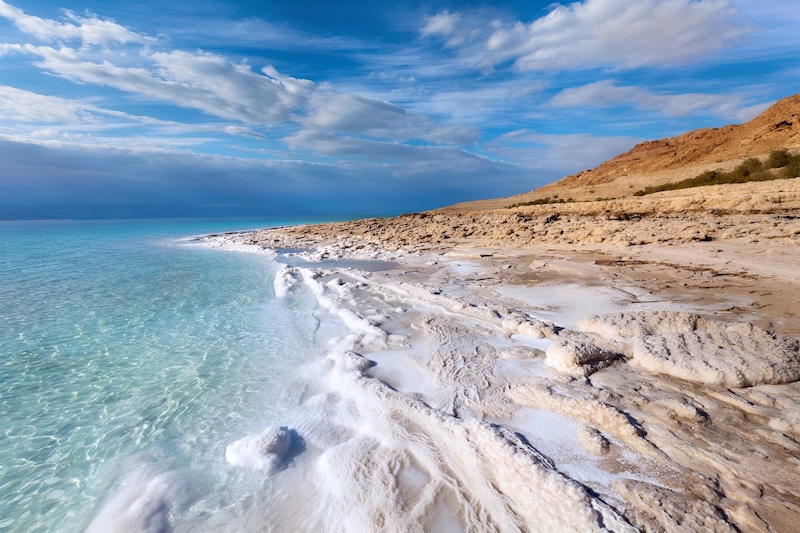 Calm shoreline of the Dead Sea with salt formations and desert mountains