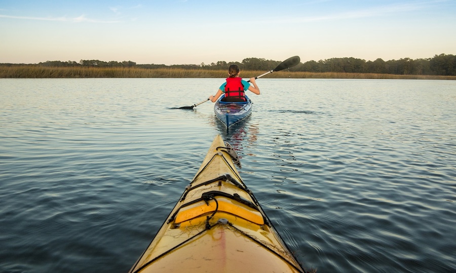 Kayakers paddling through calm Lowcountry marsh water at sunset