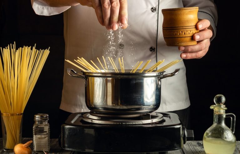 Chef seasoning pasta water with salt during cooking