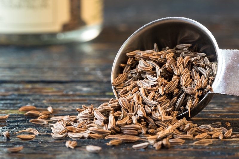 Caraway seeds spilled from wooden spoon on table